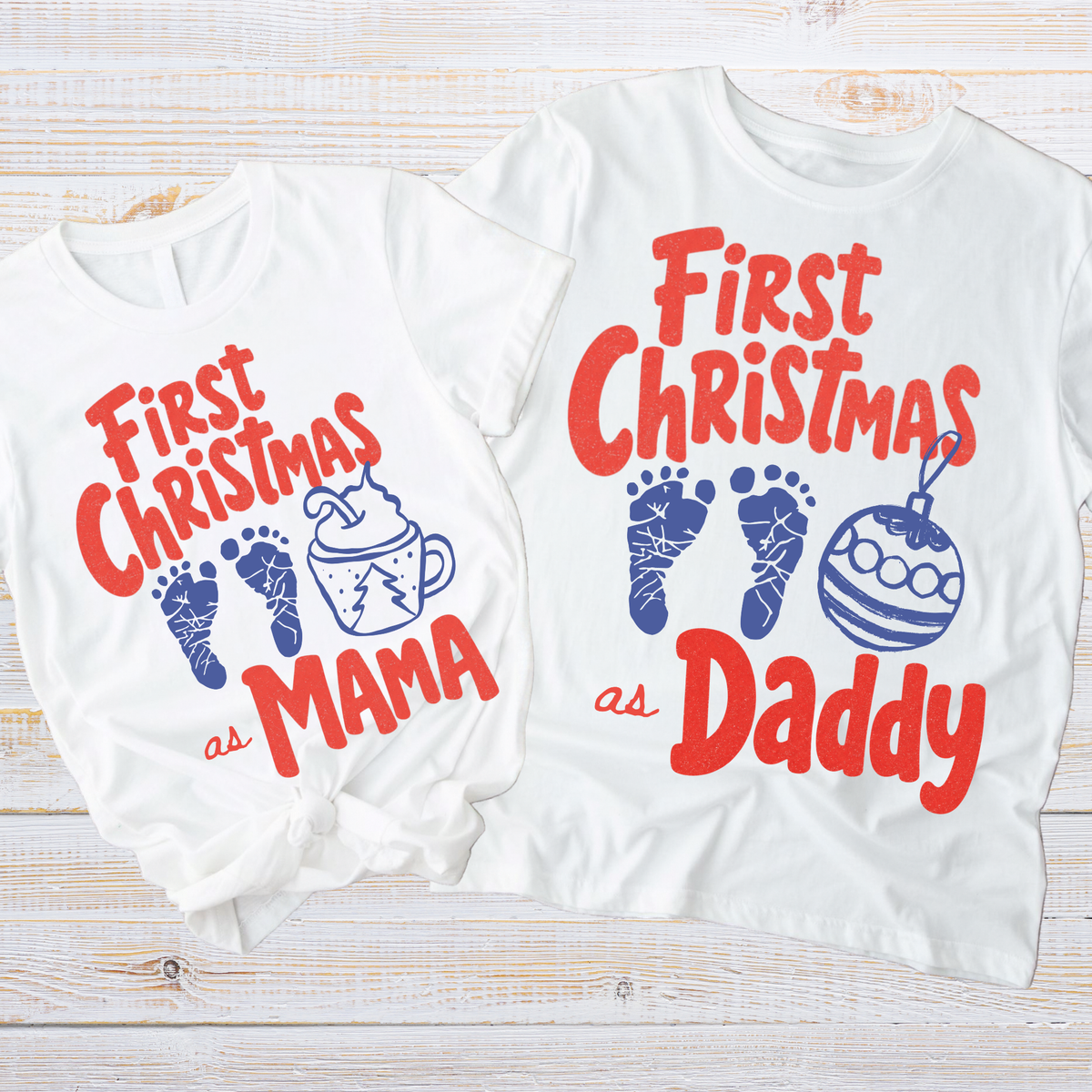 Two white graphic T-shirts laid flat on a light wood surface. The smaller shirt reads 'First Christmas as Mama' with blue footprint and mug illustrations, and the larger shirt reads 'First Christmas as Daddy' with blue footprint and ornament illustrations.