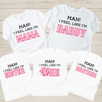 Five white graphic T-shirts arranged on a light wood background, each with different printed family-friendly slogans in black and pink: MAN! I FEEL LIKE I'M MAMA, DADDY, ONE, and BROTHER.